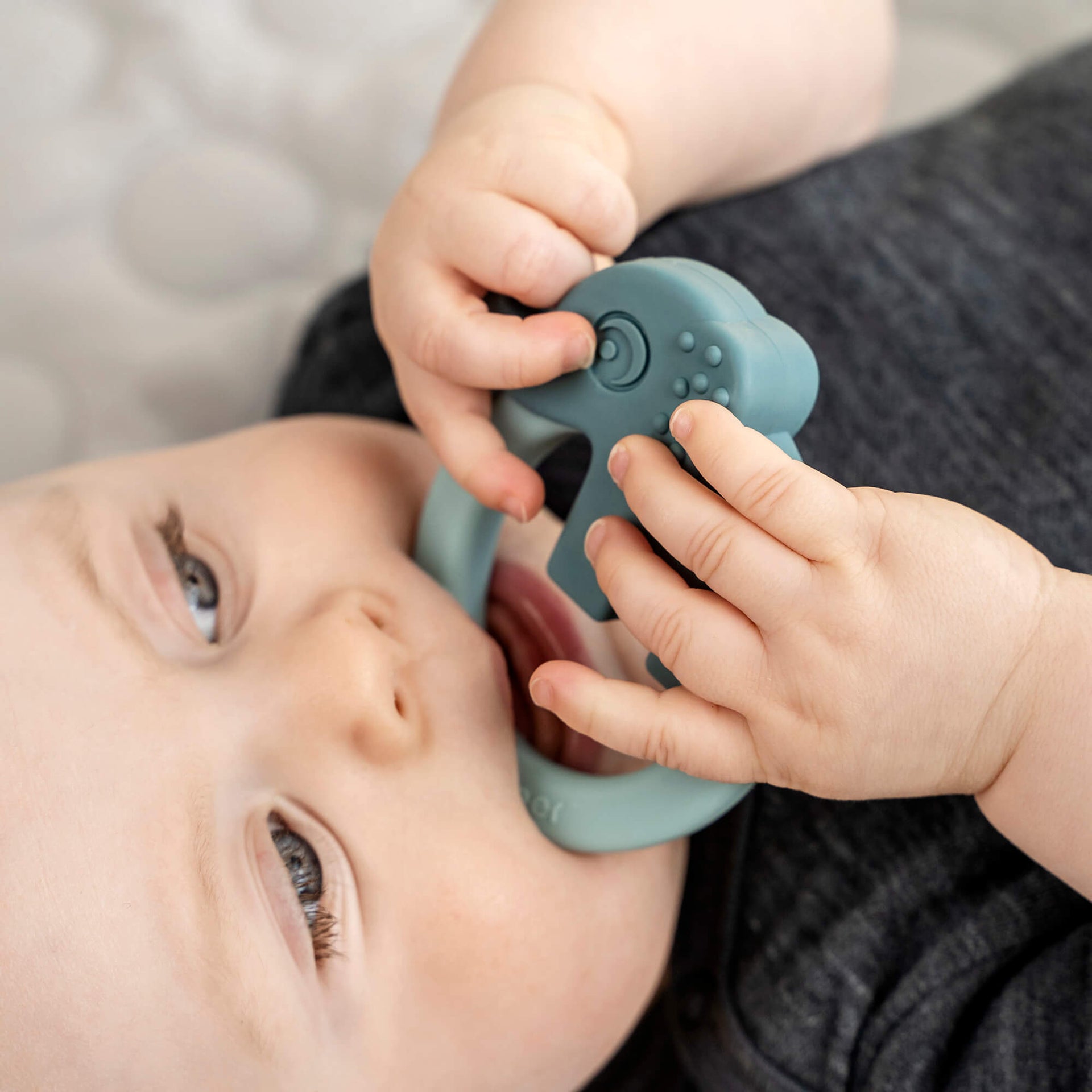 Baby liegt entspannt auf dem Rücken und kaut auf einem blauen Beißring in Form eines Tieres aus der Babylions Kollektion.