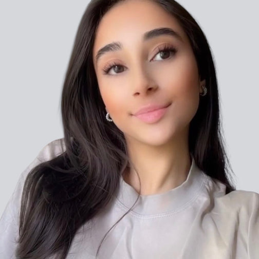 Porträtfoto der Verantwortlichen für Design und Social Media bei BabyLions mit langen dunklen Haaren und grauem Oberteil vor einfarbig grauem Hintergrund – kreative Vorstellung im Teamprofil.