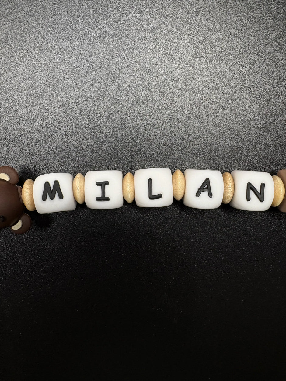 Nahaufnahme der personalisierten Schnullerkette Bär mit Namen von BabyLions® mit weißen Namensperlen, naturfarbenen Holzlinsen und Silikonperlen in Braun- und Beigetönen