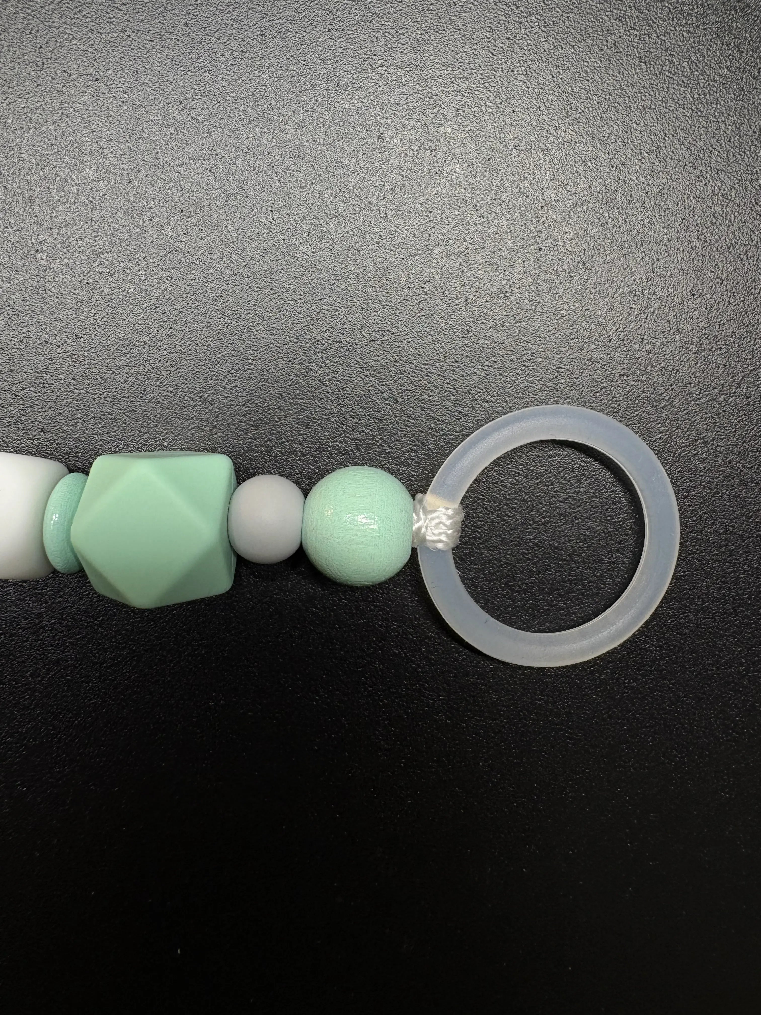 Nahaufnahme des Silikonrings der personalisierten Schnullerkette Dino mit Namen von BabyLions® mit mintfarbener Silikonperle, Holzperle und hochwertigem Schnulleradapter