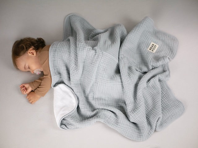 Schlafendes Baby unter grauer Musselin-Babydecke mit weicher Fleece-Innenseite – warm, atmungsaktiv und ideal für Bett, Kinderwagen und unterwegs