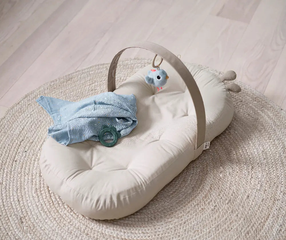 Baby Nest mit Aktivitätsbogen Raffi Done by Deer auf Spielmatte mit Babyzubehör in ruhiger Umgebung