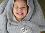 Glückliches Kind eingekuschelt in graue Musselin-Babydecke von Bearfoot – weiche, atmungsaktive Babydecke für Neugeborene und Kleinkinder