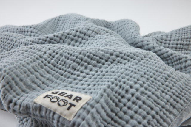 Detailaufnahme der grauen Musselin-Babydecke mit Bearfoot-Label – weiche, atmungsaktive Struktur für Neugeborene und Kleinkinder