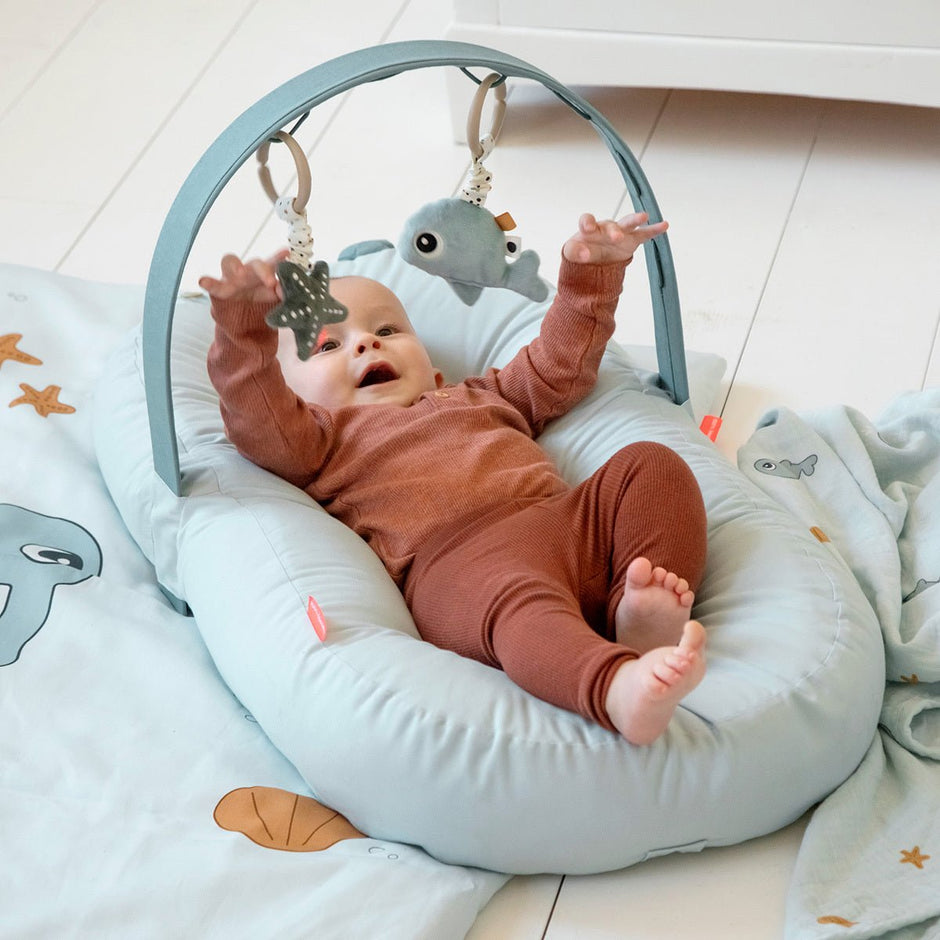Baby spielt mit Hängespielzeug Wally und Seestern am Aktivitätsbogen auf weicher Spielunterlage