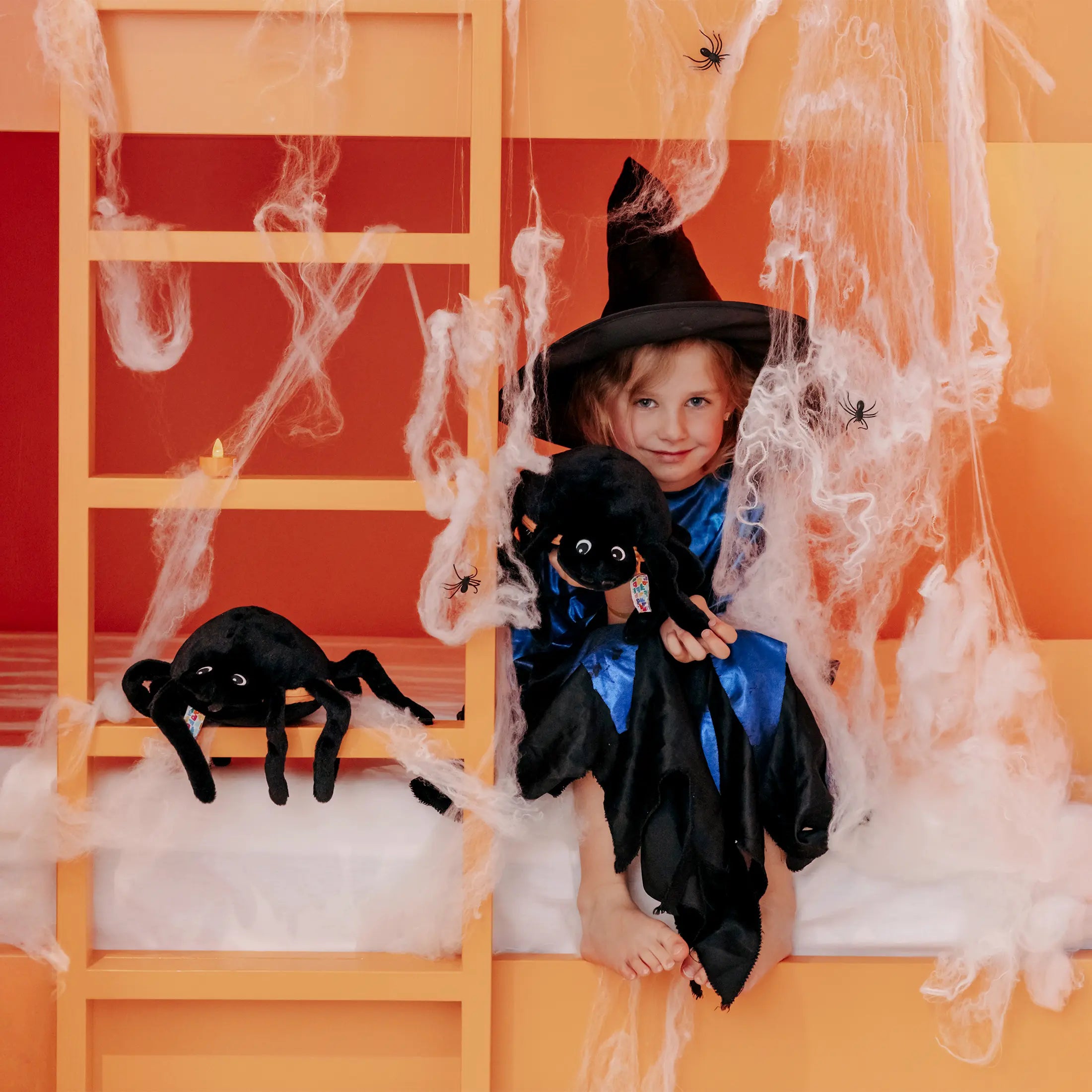 Kind im Hexenkostüm spielt mit schwarzem Spinnen Kuscheltier in Halloween Dekoration