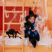 Kind im Hexenkostüm spielt mit schwarzem Spinnen Kuscheltier in Halloween Dekoration