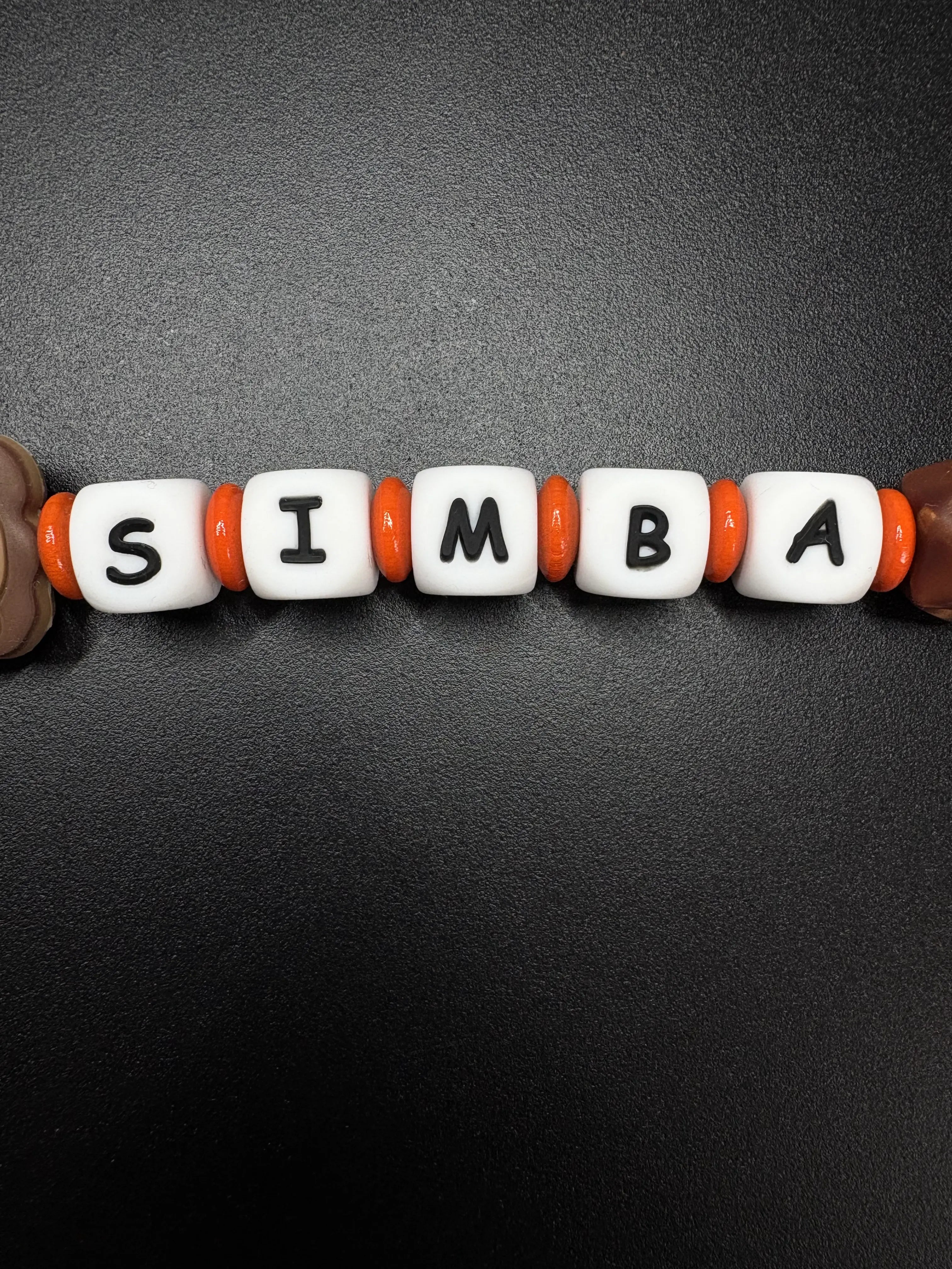 Detailaufnahme der personalisierten Schnullerkette Simba mit weißen Namensperlen und orangefarbenen Silikonringen