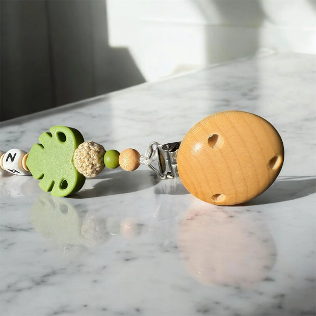 Detailaufnahme einer Schnullerkette mit Holzclip, grünen Perlen und Blatt-Element
