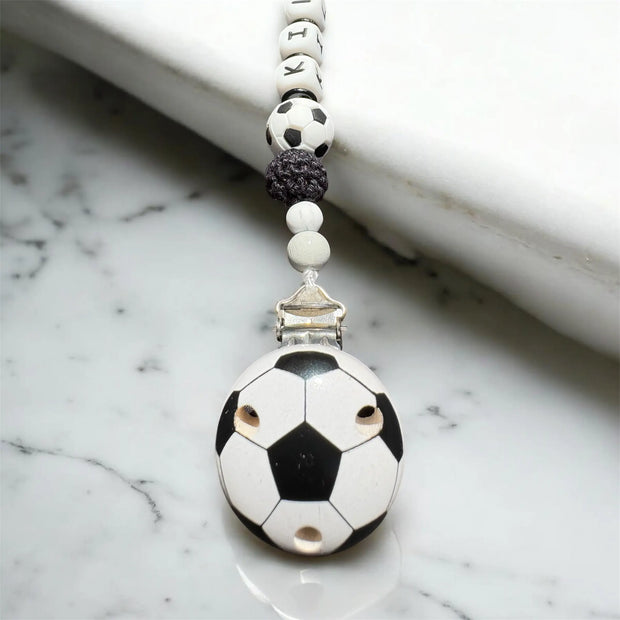 Nahaufnahme einer Schnullerkette mit Fußball-Holzclip in Schwarz Weiß
